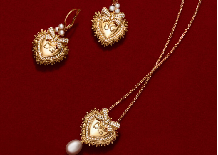 Dolce & Gabbana gold heart earrings and a heart pendant necklace with a pearl on red fabric