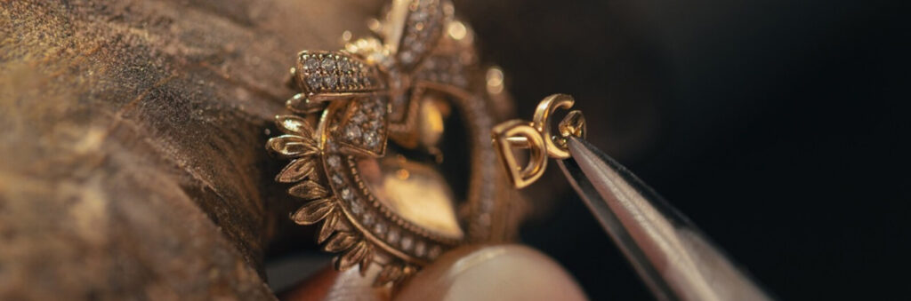 Dolce & Gabbana close-up of a gold heart jewellery piece set with diamonds, held with tweezers