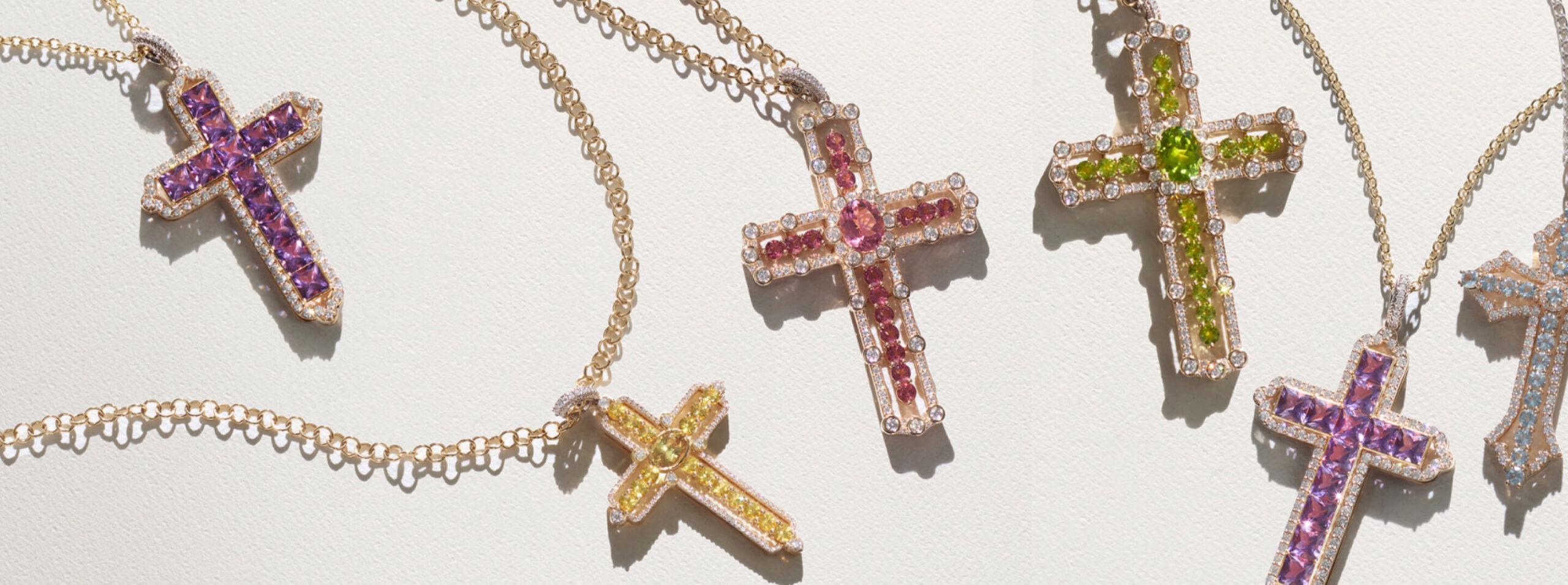 Dolce & Gabbana gold crosses set with purple, pink, green, yellow and blue gemstones on delicate chains, laid on a pale surface