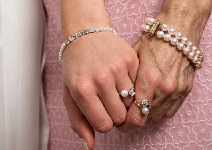 IMPERIAL Pearl pearl bracelets and rings on clasped hands against pink floral fabric