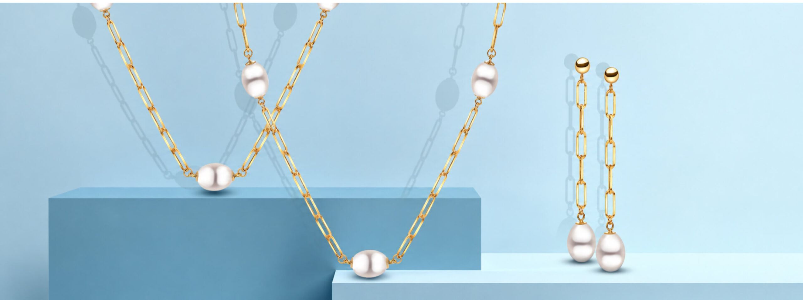 IMPERIAL Pearl gold paperclip-chain necklaces with large pearls and matching pearl drop earrings on a pale blue backdrop